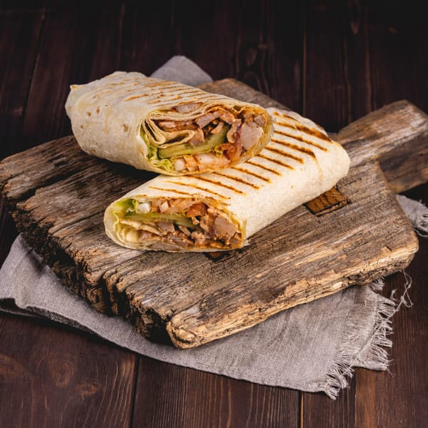 Two grilled Gyro King chicken shawarmas, cut in half, on a rustic wooden board and linen.