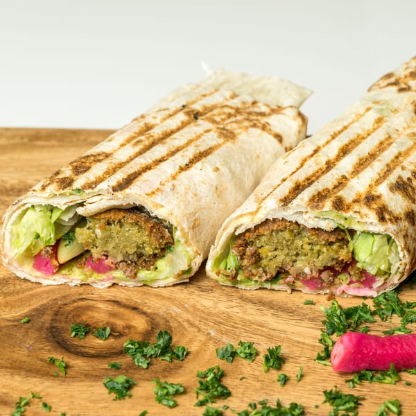 Two grilled falafel wraps with lettuce, pickled vegetables, and parsley on a wooden board.