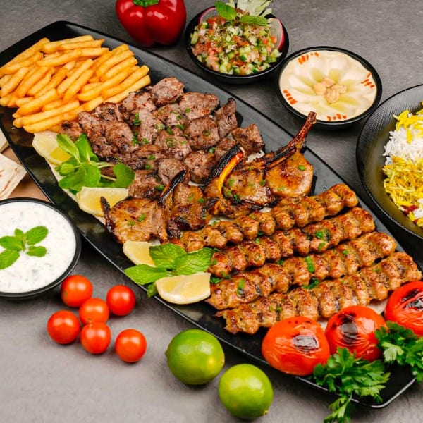 A large platter of Mediterranean grilled meats, fries, rice, hummus, salad, and sauces.