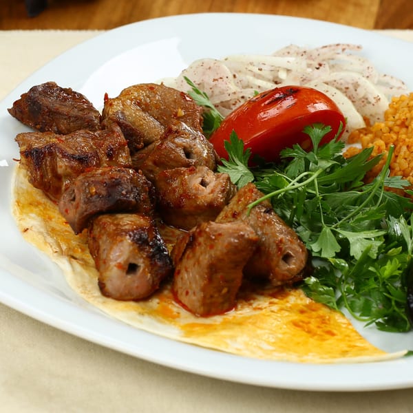 Gyro King Grill's Mediterranean shish kebab with grilled tomato, onions, parsley, and bulgur on a white plate.