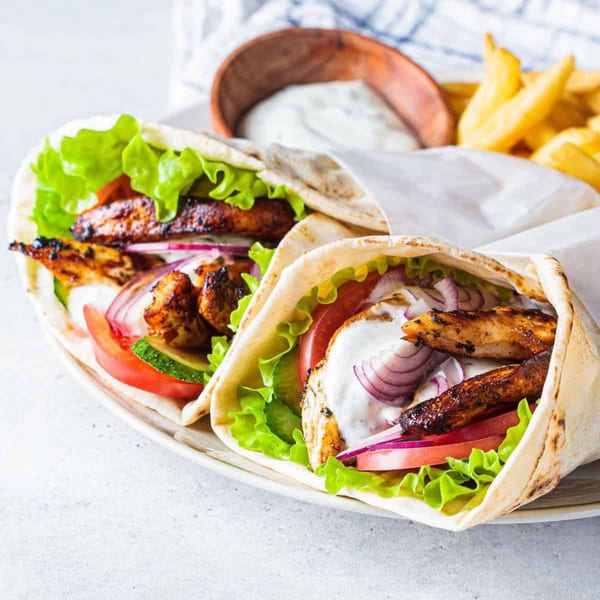 Two chicken gyros with lettuce, tomato, onion, and sauce, served with fries and dip.