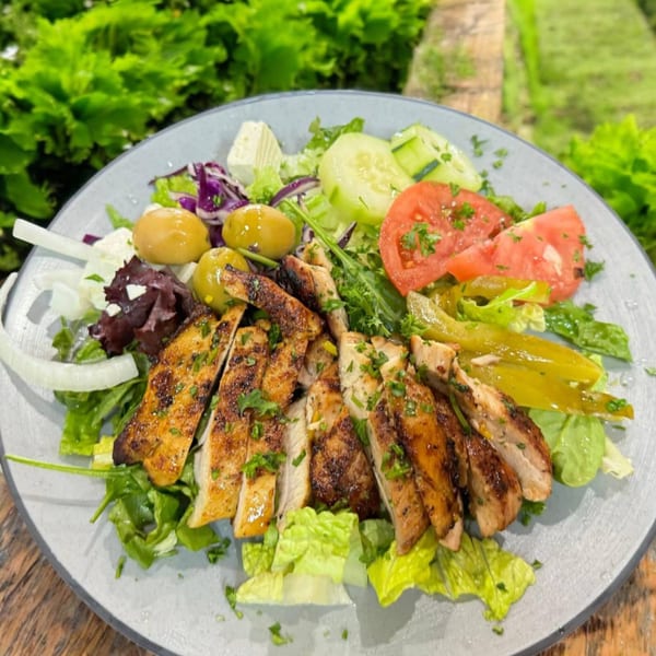 Mediterranean salad with grilled chicken, olives, feta, tomatoes, cucumbers, and peppers on a gray plate.