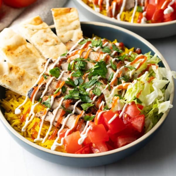 Gyro King Grill's chicken rice bowl with pita bread, lettuce, tomatoes, and sauces.