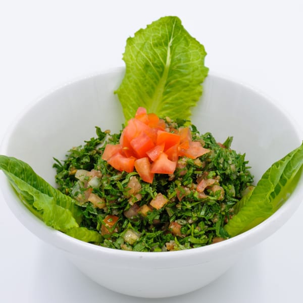 A white bowl filled with green tabbouleh salad, garnished with diced tomatoes and lettuce leaves.